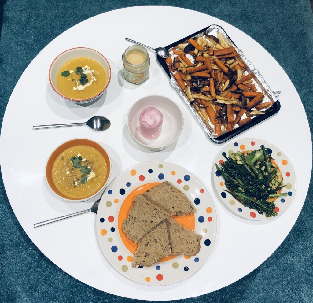 Top down image of the final meal, featuring two bowls of soup, bread, the roasted vegetables, and cooked greens.