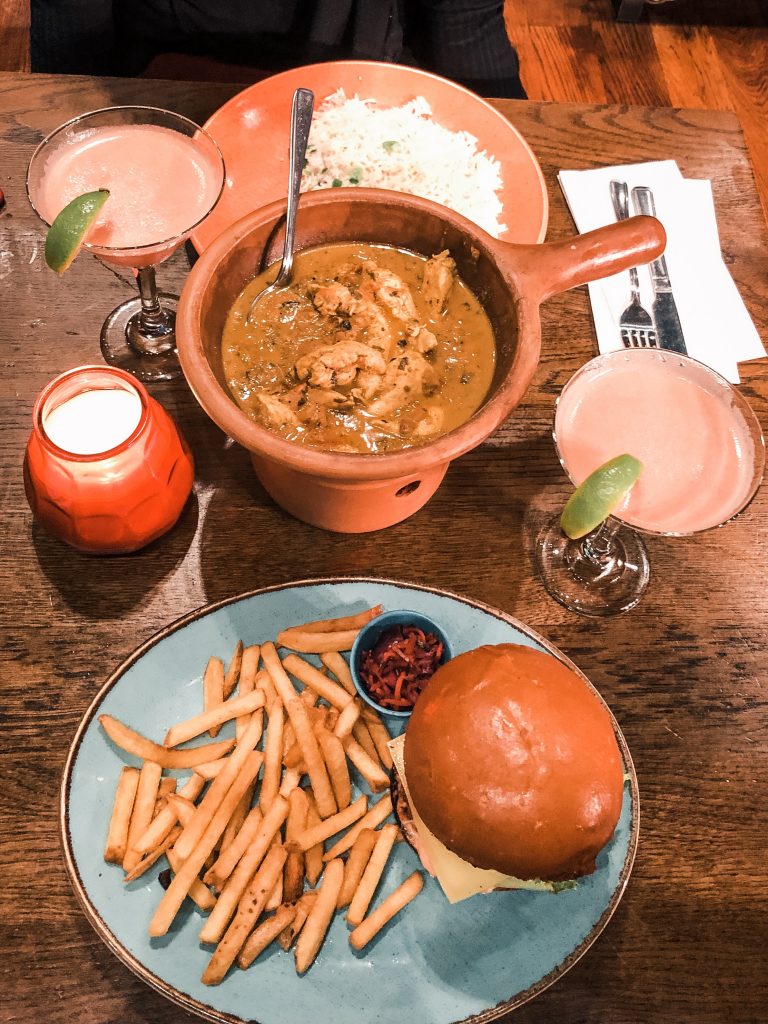 A photo of two mains, a burger and chips and a pot of Coconut Chicken Curry from Las Iguanas.