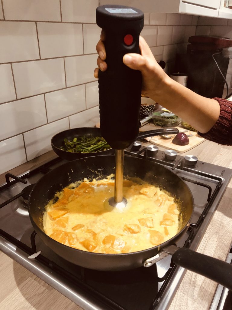Image of a hand blender blending the cooked pumpkin into the soup.