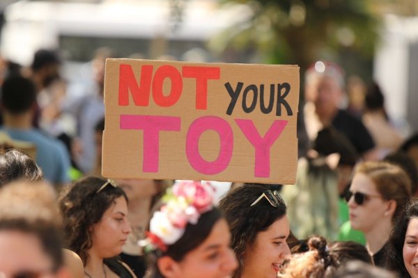 Female protesters holding a hand-drawn cardboard sign that reads 'NOT YOUR TOY'.