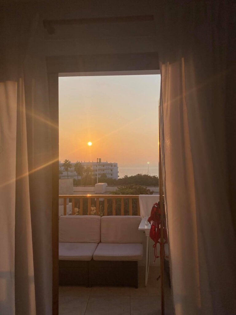 Apartment balcony with a sofa, a drying bikini, curtains in view, and sunset