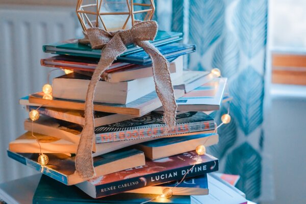 A stack of books, covered in fairy lights, with a candle on top