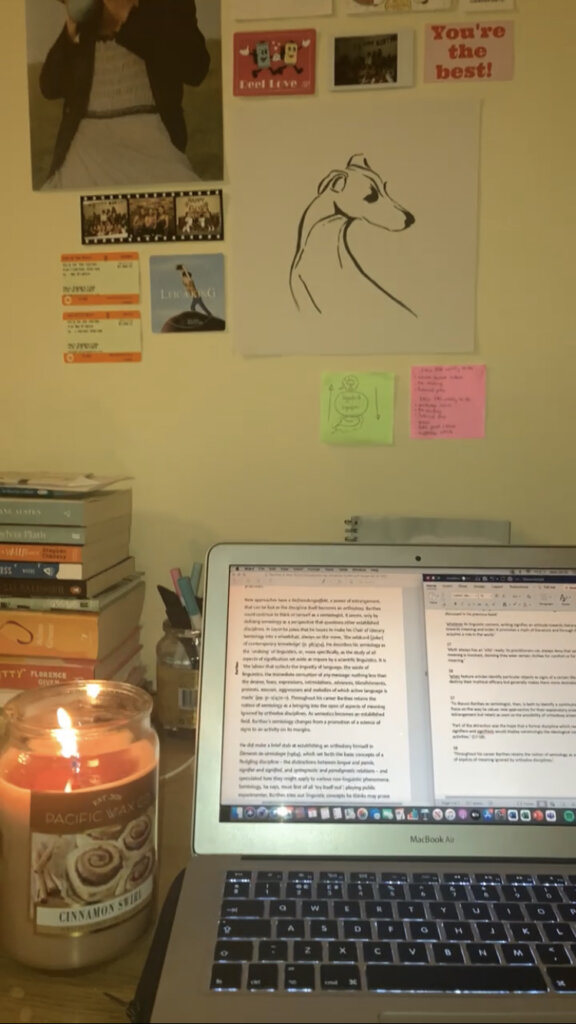 A laptop with a Word document open, a candle lit next to it, and post-it notes on the wall behind it. Aiming to show something 'that girl' would be doing