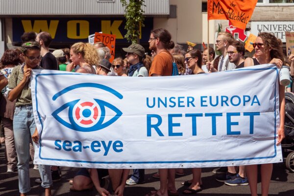 Migration protester's sign that reads "Unser Europa Rettet" and has the 'sea-eye' logo on it